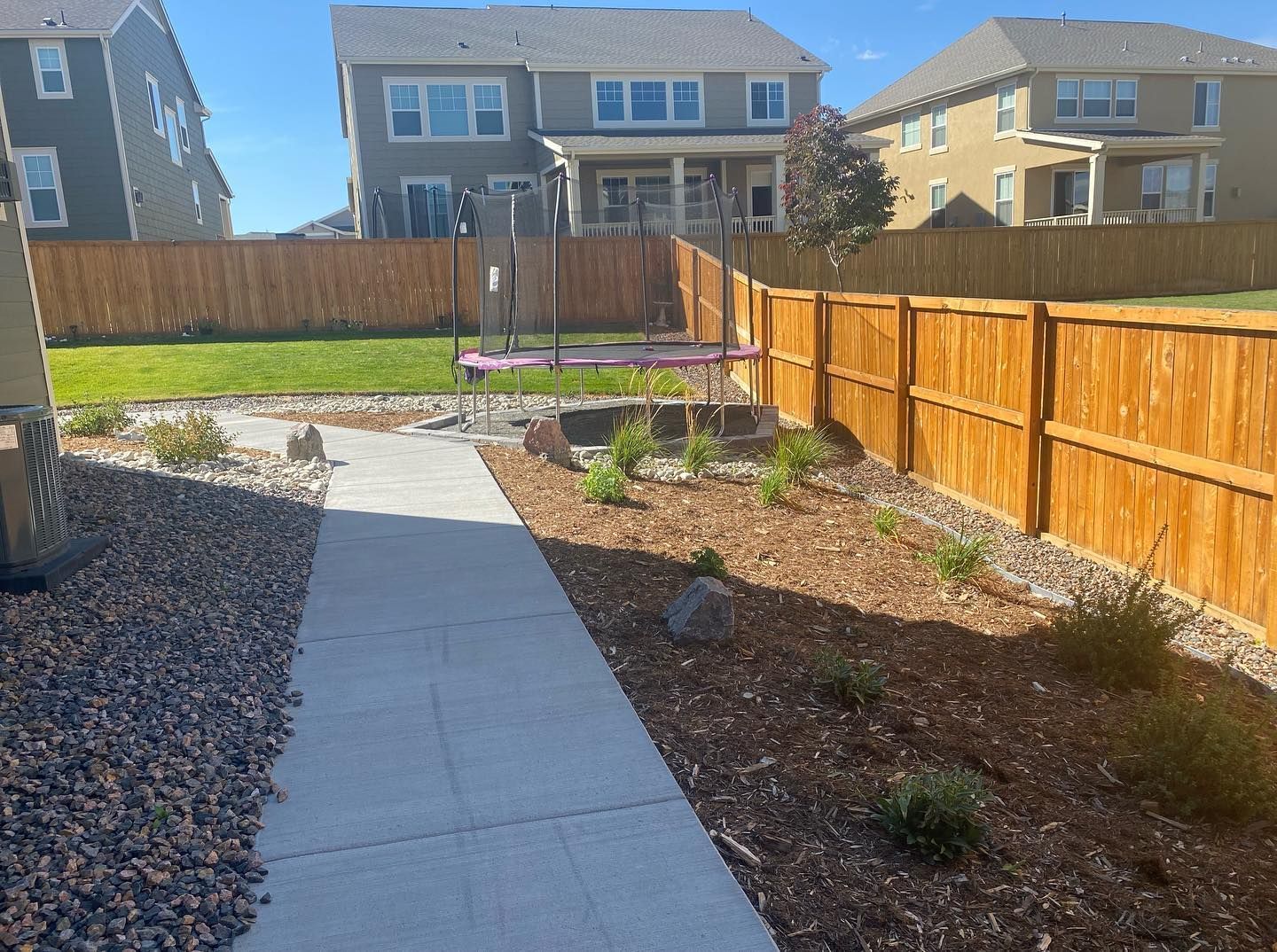 A backyard with a wooden fence, concrete path, and a playground set. 
