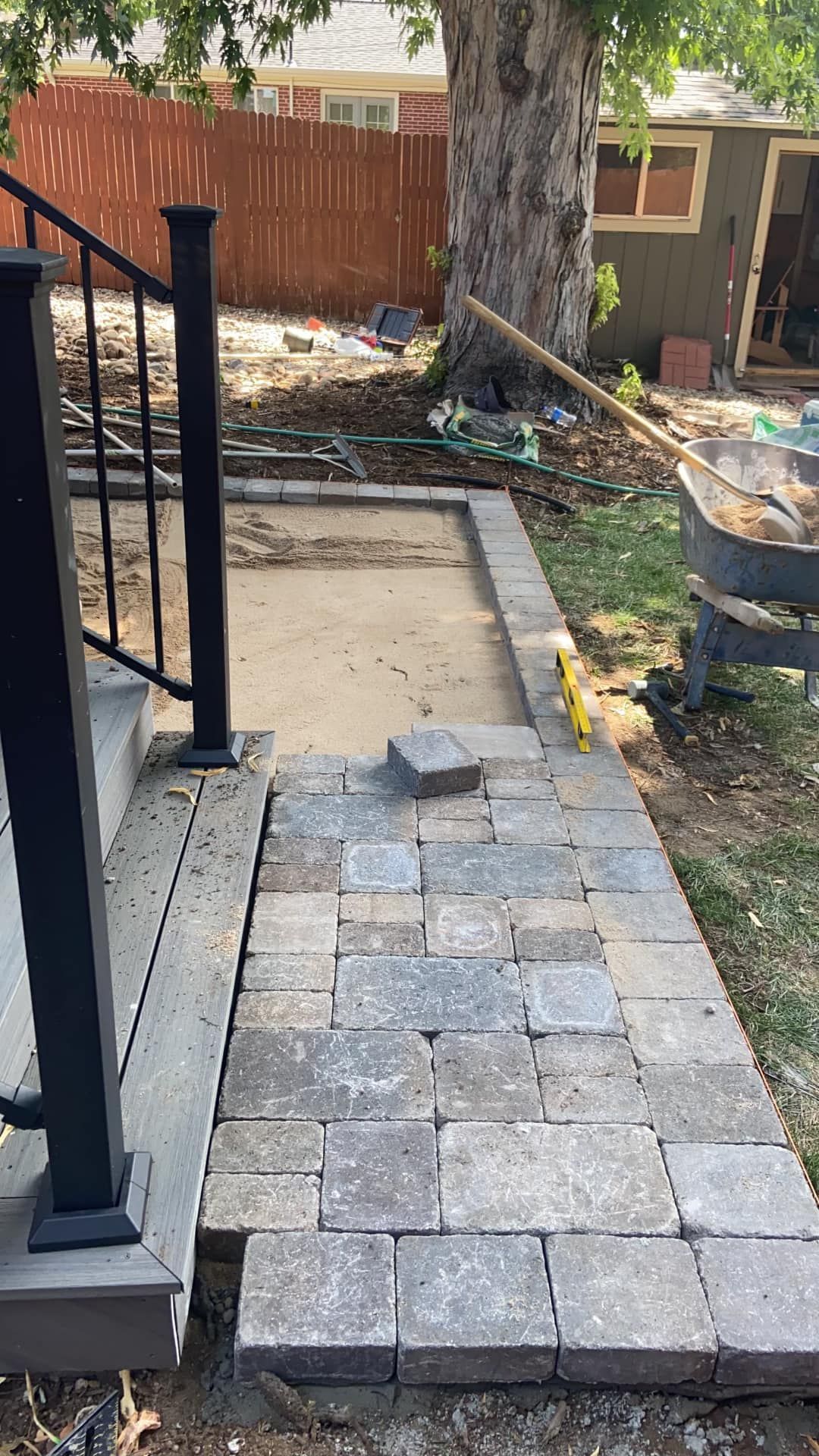 Pathway construction in progress, with pavers laid adjacent to porch steps. Brown and gray stones contrast with a dirt base.