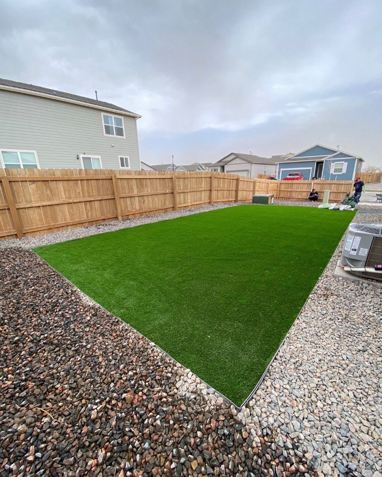 Three landscapers installing sod and paving stones in a residential backyard with a wooden fence.
