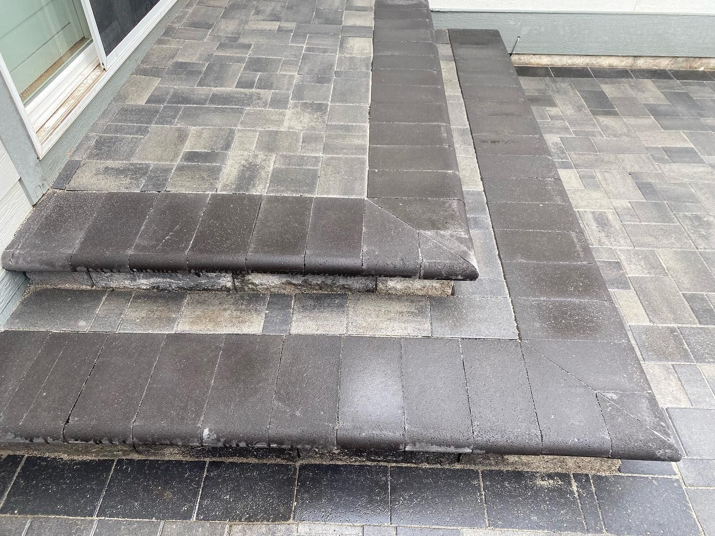 Dark brick steps leading onto a gray paved patio, with a section of matching dark brick border.
