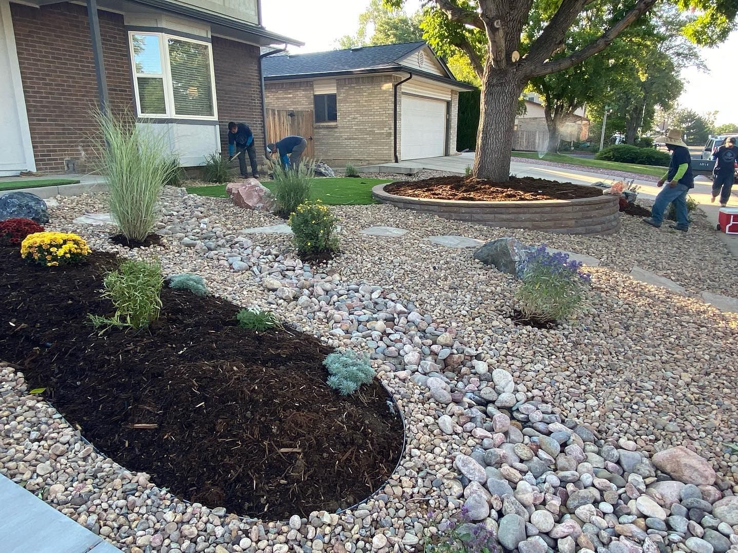 Landscapers working in a front yard with mulch, gravel, plants, and stepping stones.