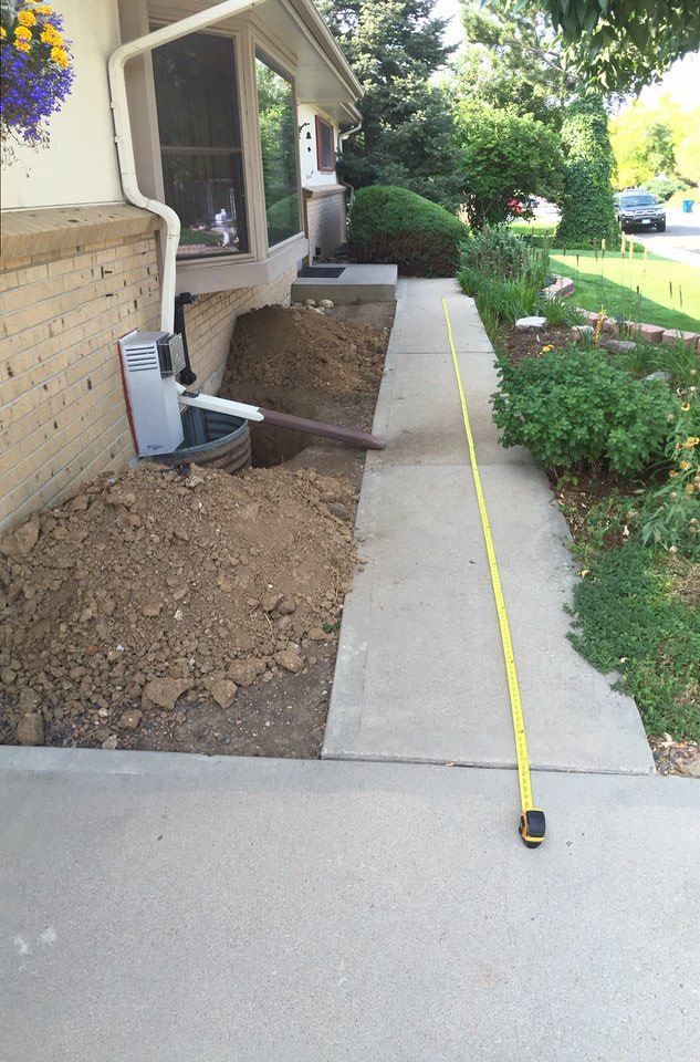 Construction site next to a sidewalk. Pile of dirt by a house, a gutter, and a measuring tape extending down the sidewalk.