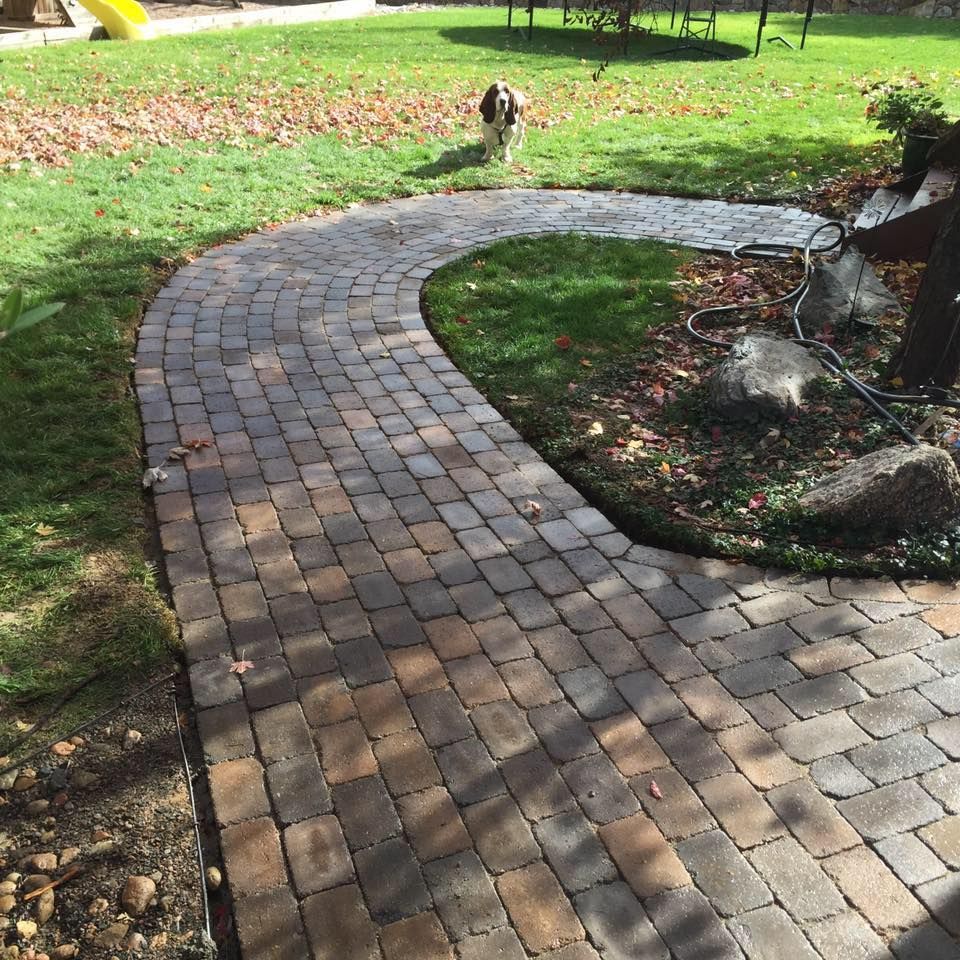 A curved brick pathway winds through a grassy yard. A dog is in the background.
