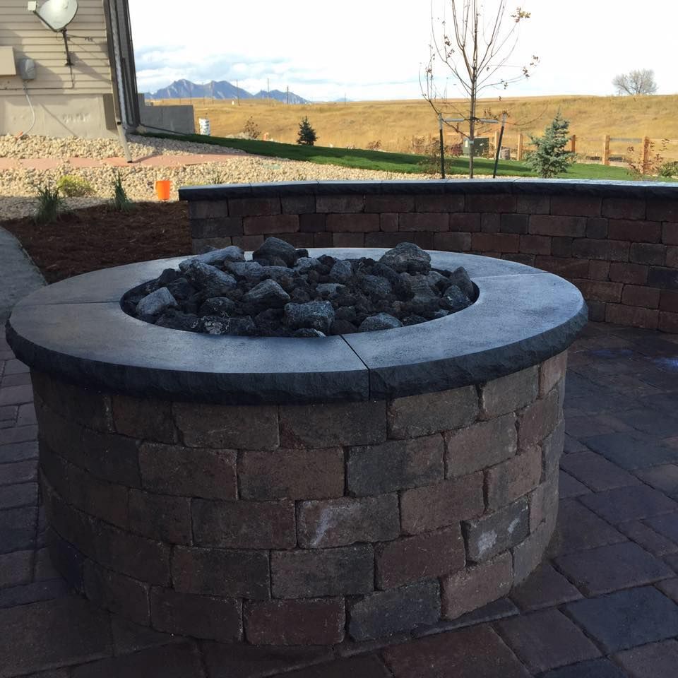 Brick fire pit with a dark stone rim and rocks inside, set on a brick patio. 