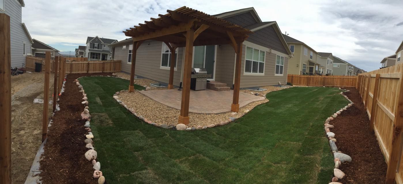 Backyard with wooden pergola, green lawn, stone pathway, and wooden fence. Cloudy sky.