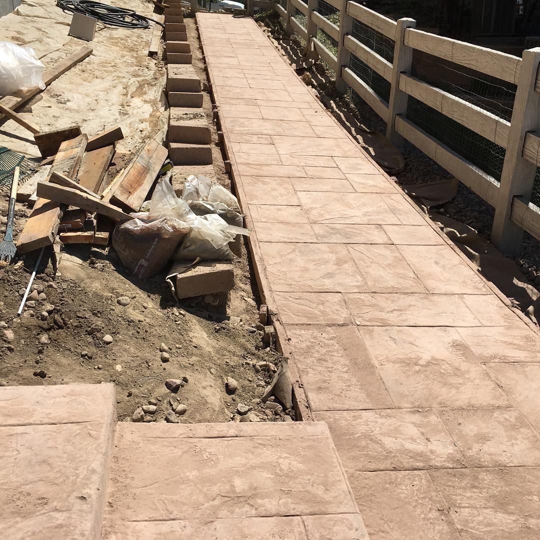 A stamped concrete walkway with steps under construction next to a wooden fence. Debris and tools are scattered nearby.