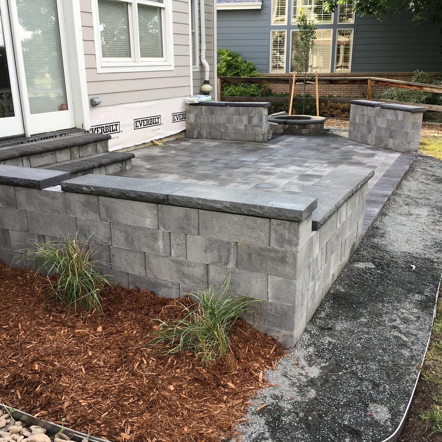 Gray block patio with raised seating, fire pit, and mulch landscaping.