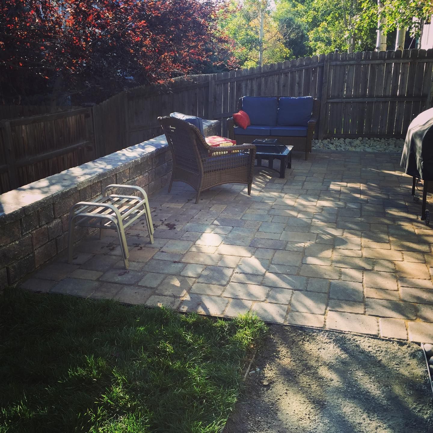 Patio with paved stones, seating area, and a wall. There is a sofa, chair, and small table.