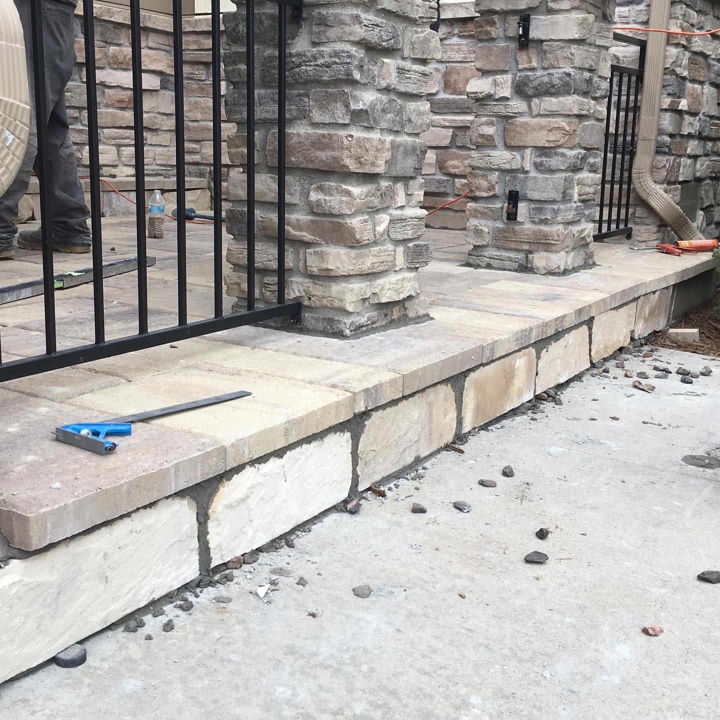 Stone retaining wall with a black metal fence. A blue measuring tool rests on the wall’s top surface.