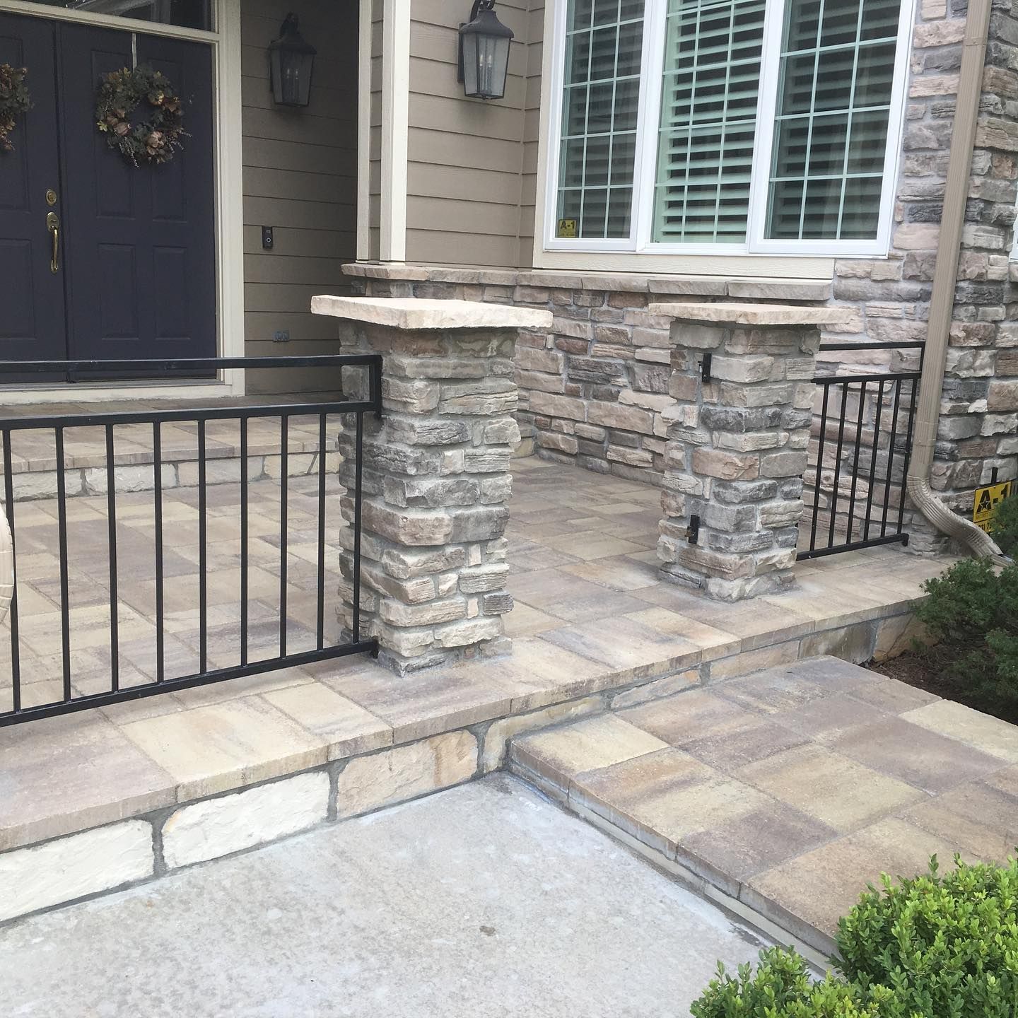 Stone porch and walkway with black railing and columns in front of a house with a dark blue door.