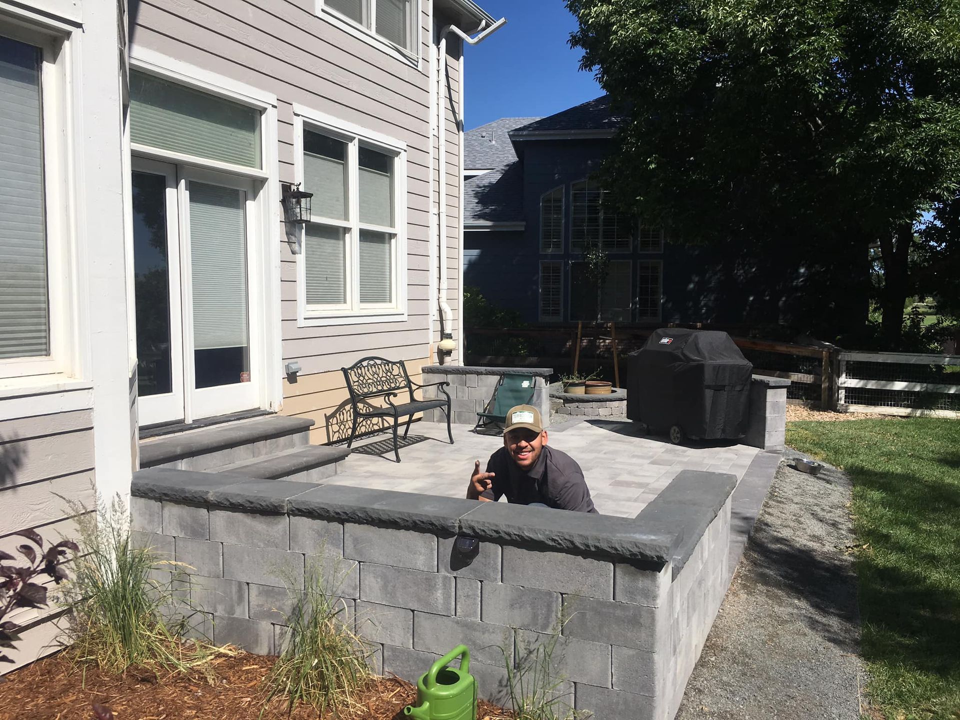 Man giving a thumbs-up from a built-in patio with gray block walls. The patio is next to a house.