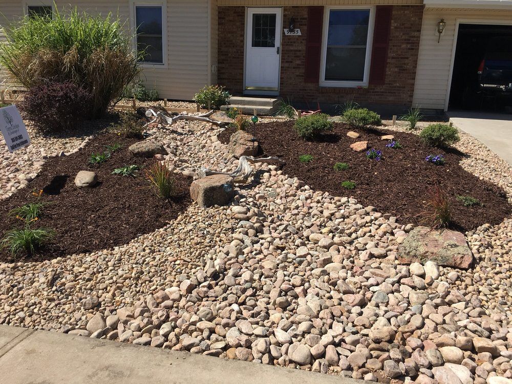 Landscaped front yard with a rock bed and mulch pathways leading to the front door of a brick house.