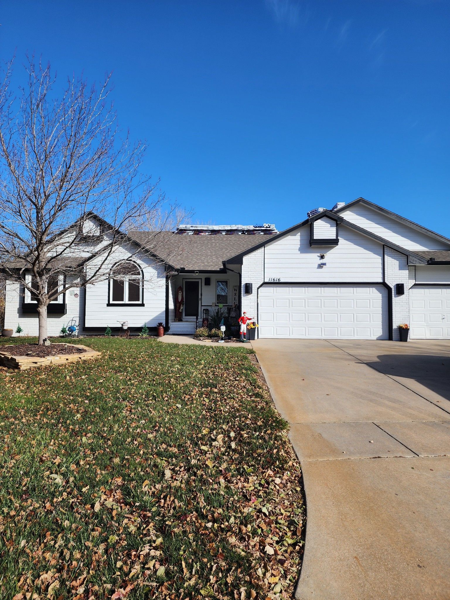 A white house with a driveway and a tree in front of it.
