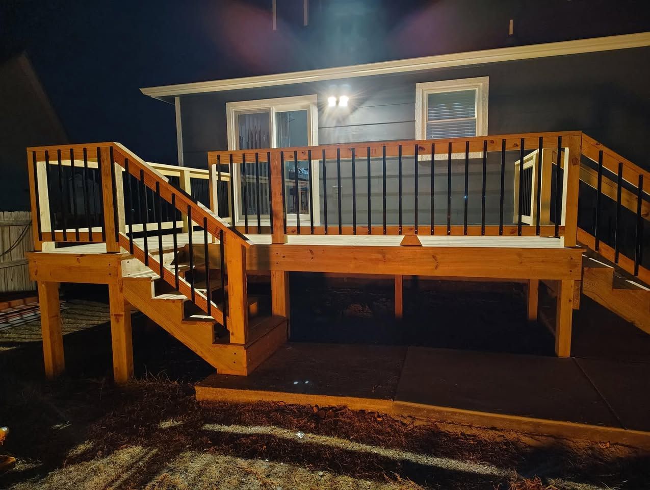 A wooden deck with stairs leading up to it is in front of a house at night.