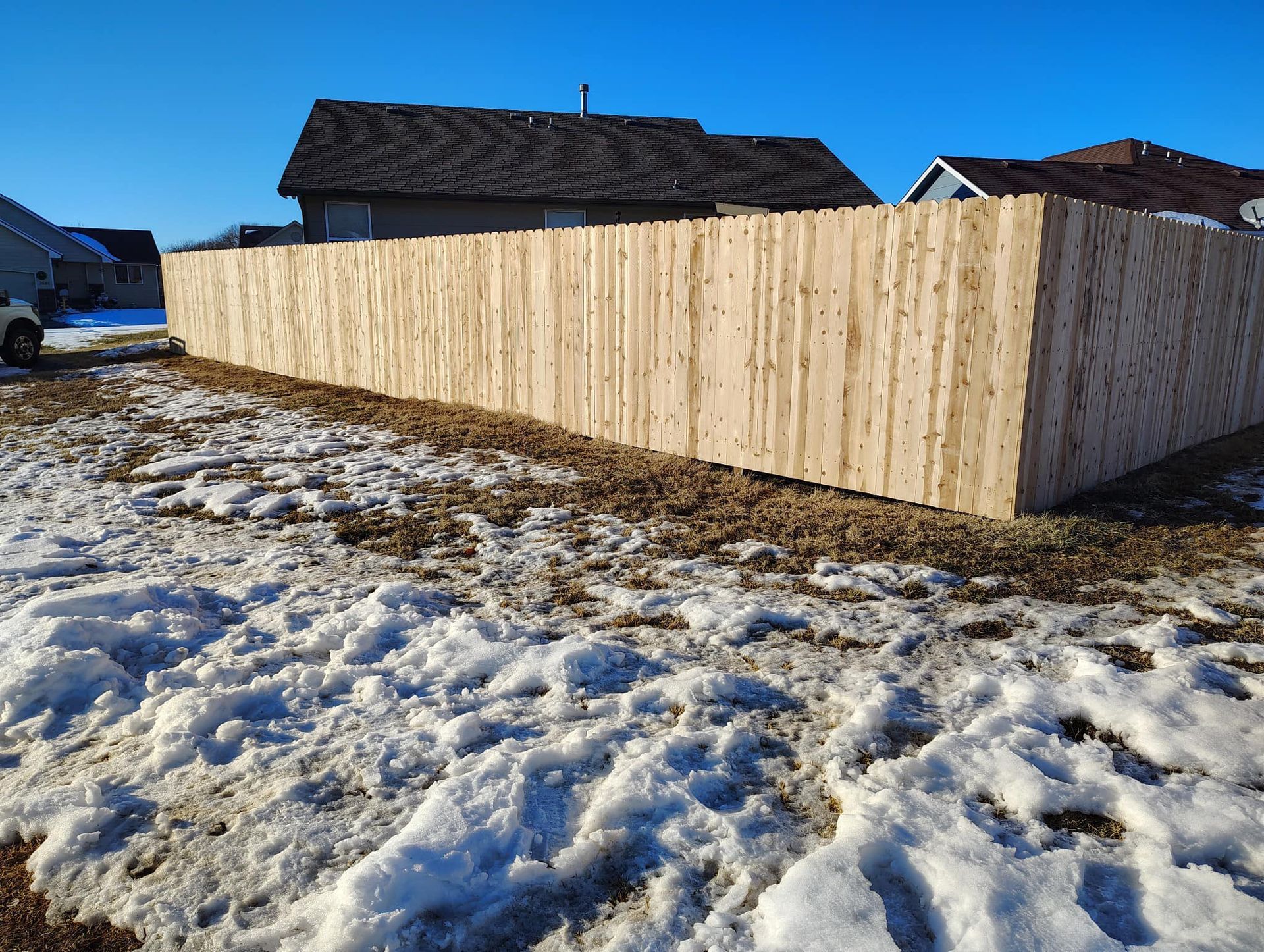 A wooden fence is sitting in the snow in front of a house.