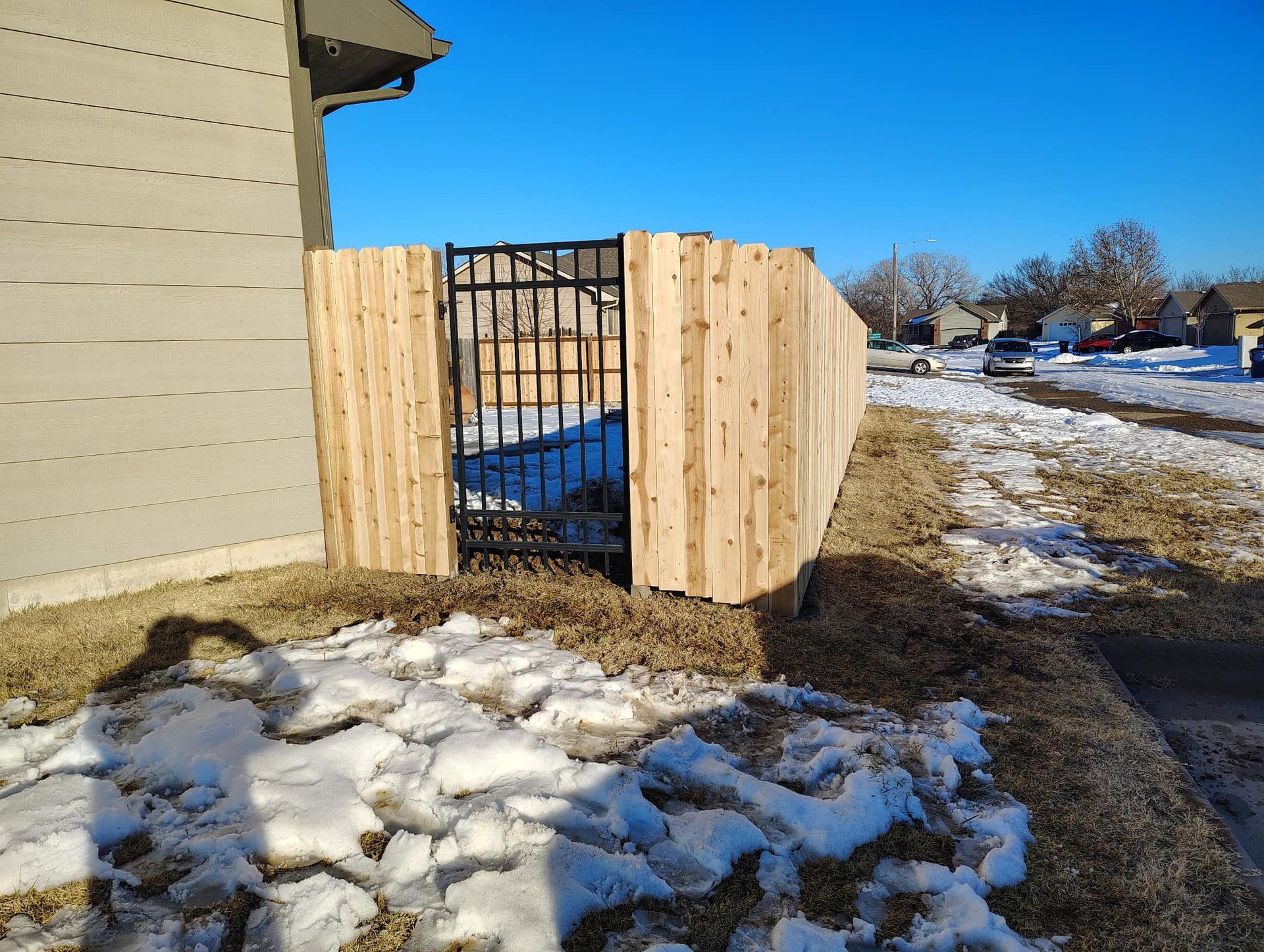 A wooden fence with a gate in the snow next to a house.