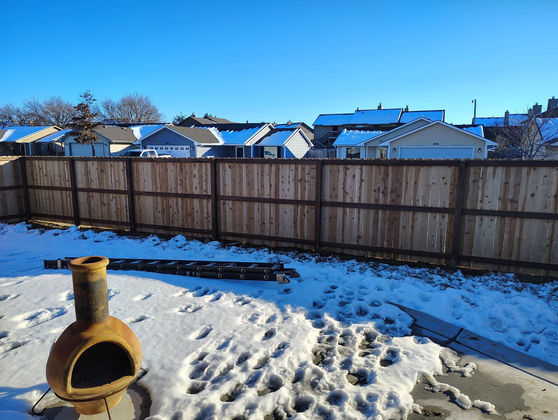 A wooden fence surrounds a snowy yard with a fire pit in the foreground.