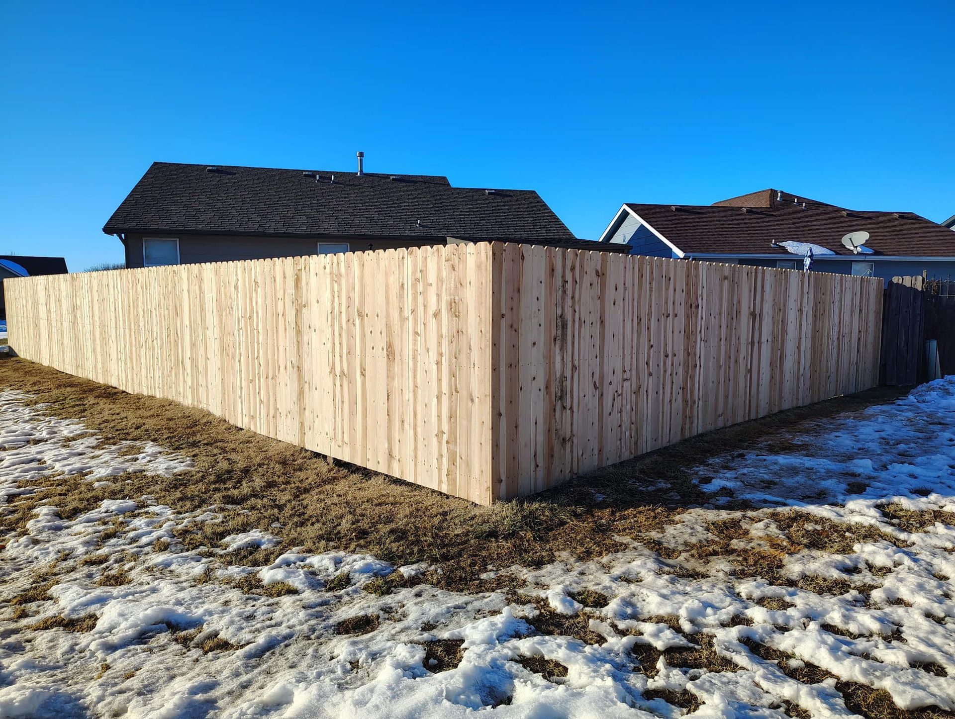 A wooden fence is in the middle of a snowy field in front of a house.