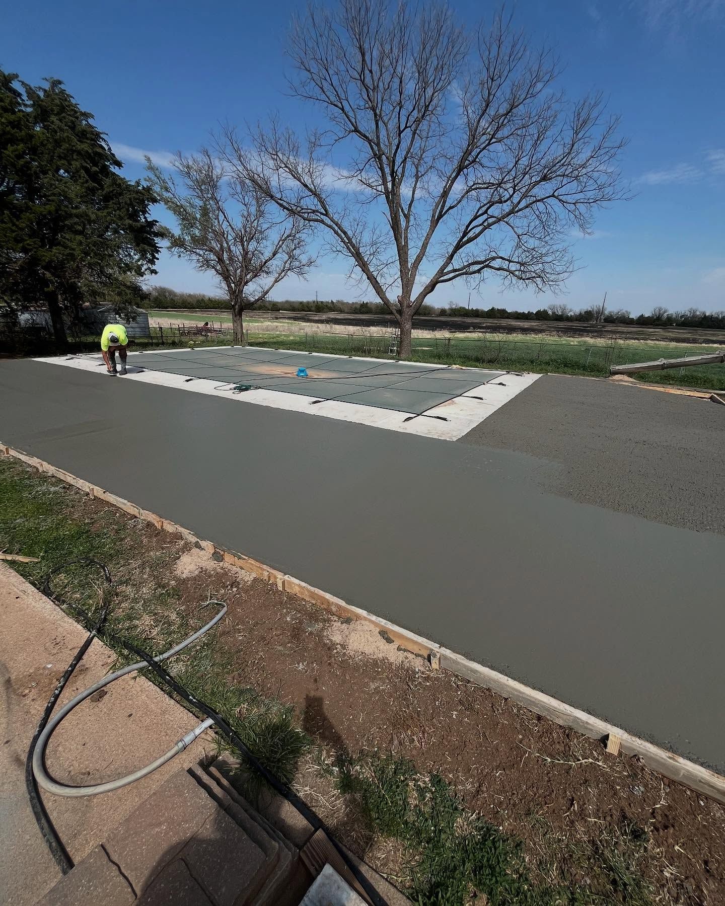 A man is working on a concrete driveway with a tree in the background.