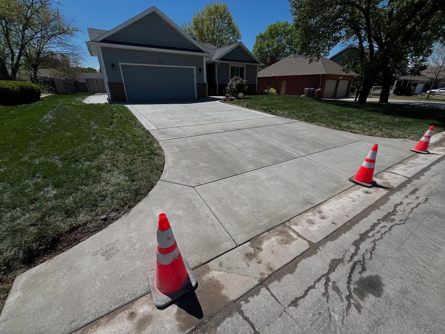 A row of traffic cones are sitting on the side of a driveway in front of a house.