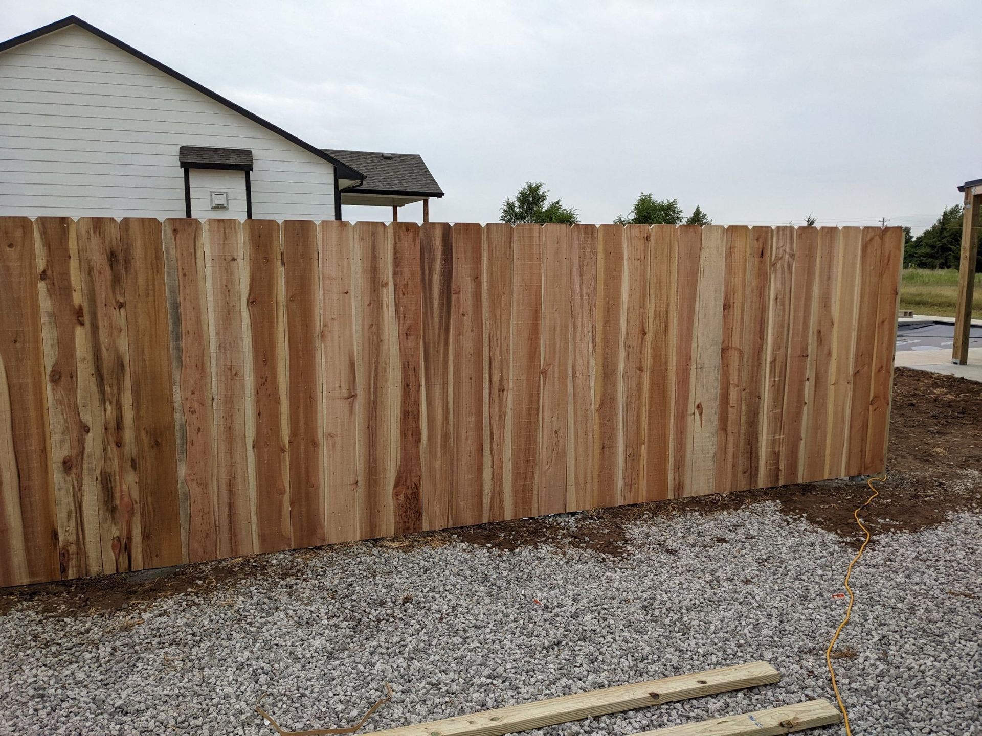 A wooden fence is sitting on top of gravel in front of a house.