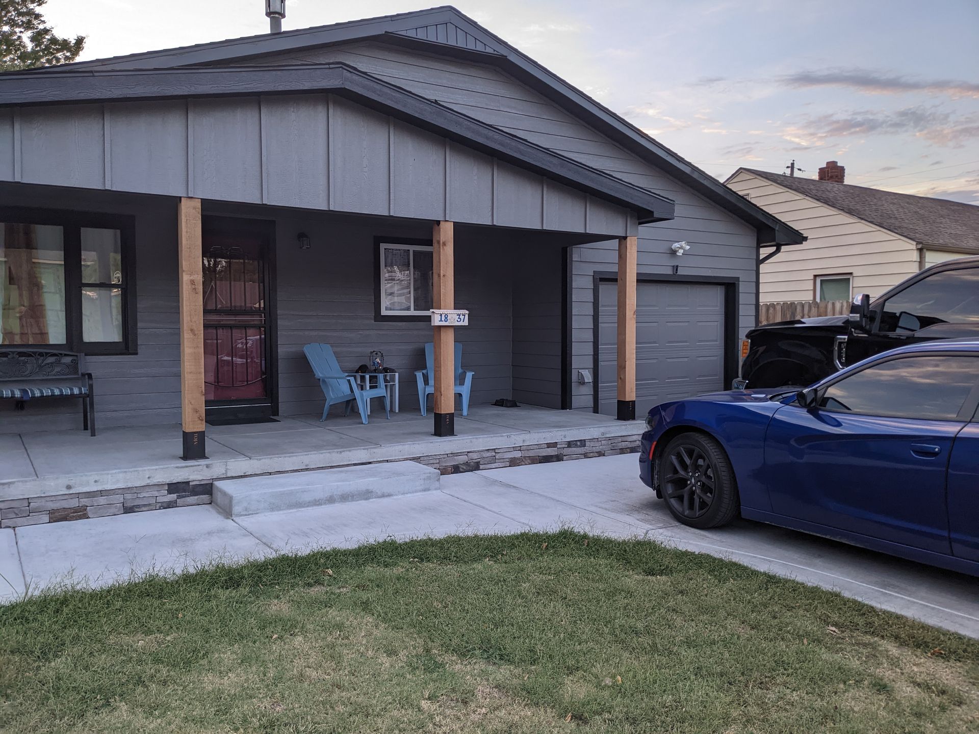 A blue car is parked in front of a house with a porch.