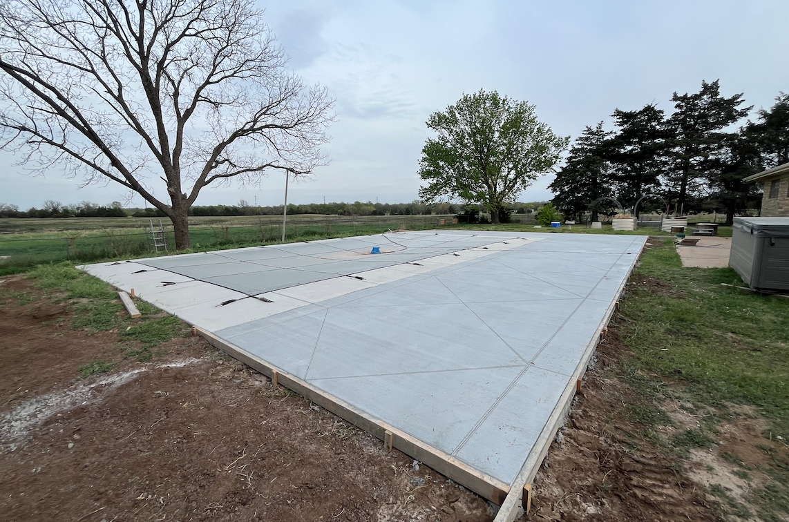 A concrete driveway is being built in a field with trees in the background.