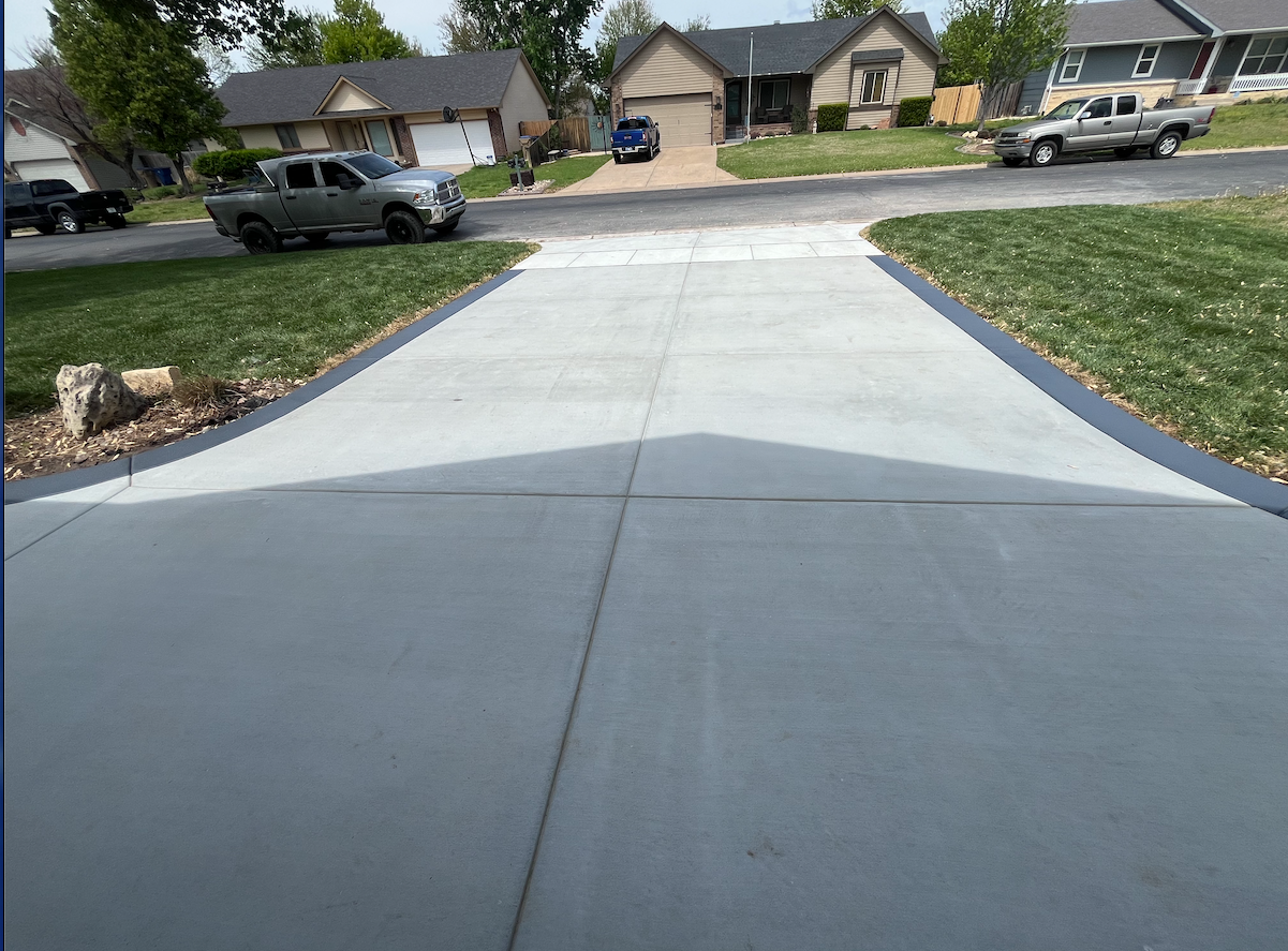 A gray truck is parked on the side of a concrete driveway.
