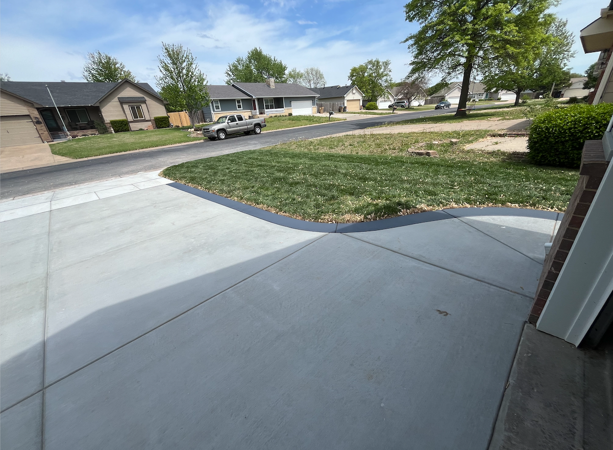 A car is driving down a residential street next to a concrete driveway.