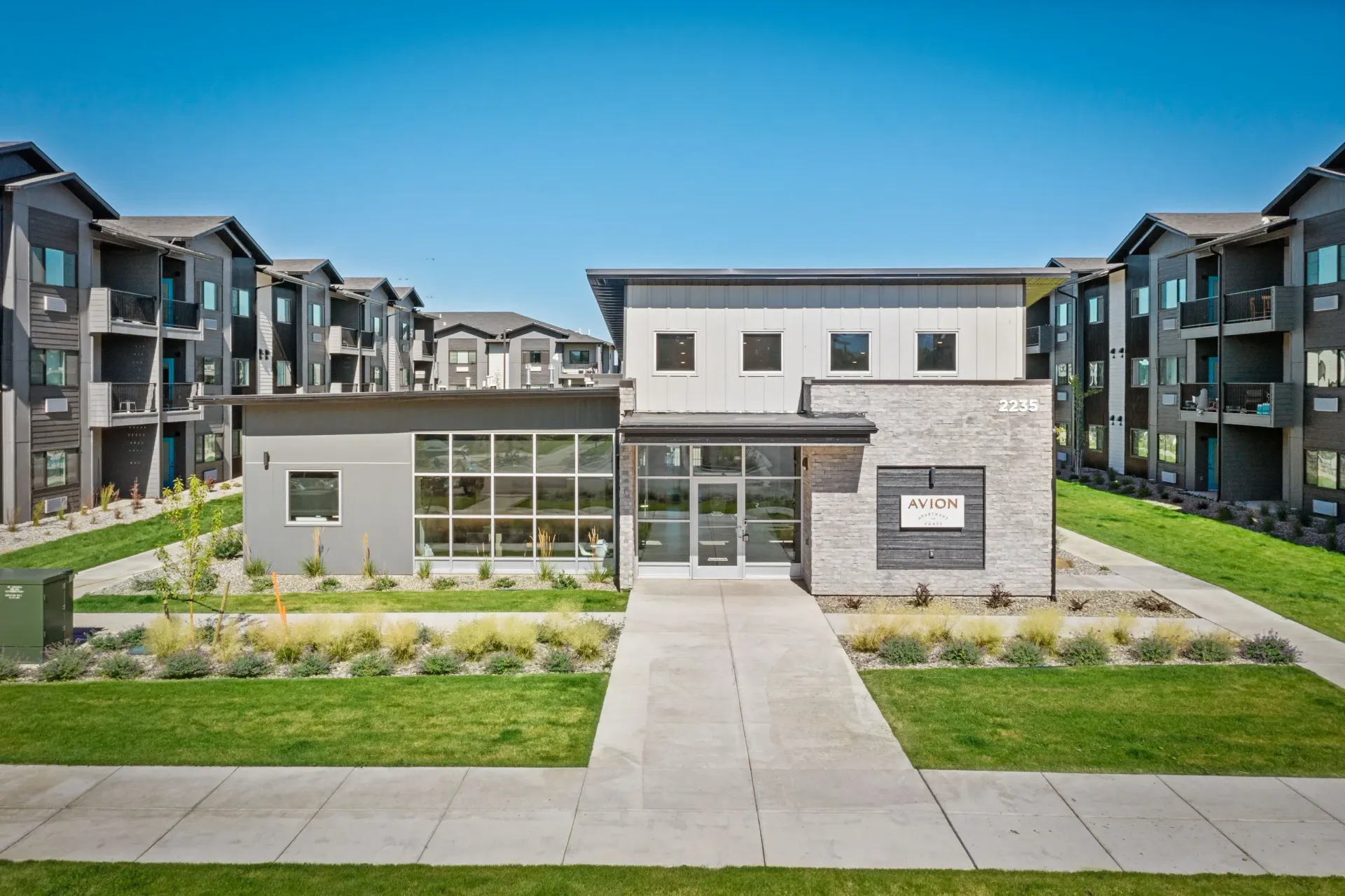 Aerial view of a modern apartment complex with a central clubhouse and surrounding buildings, landscaped grounds.