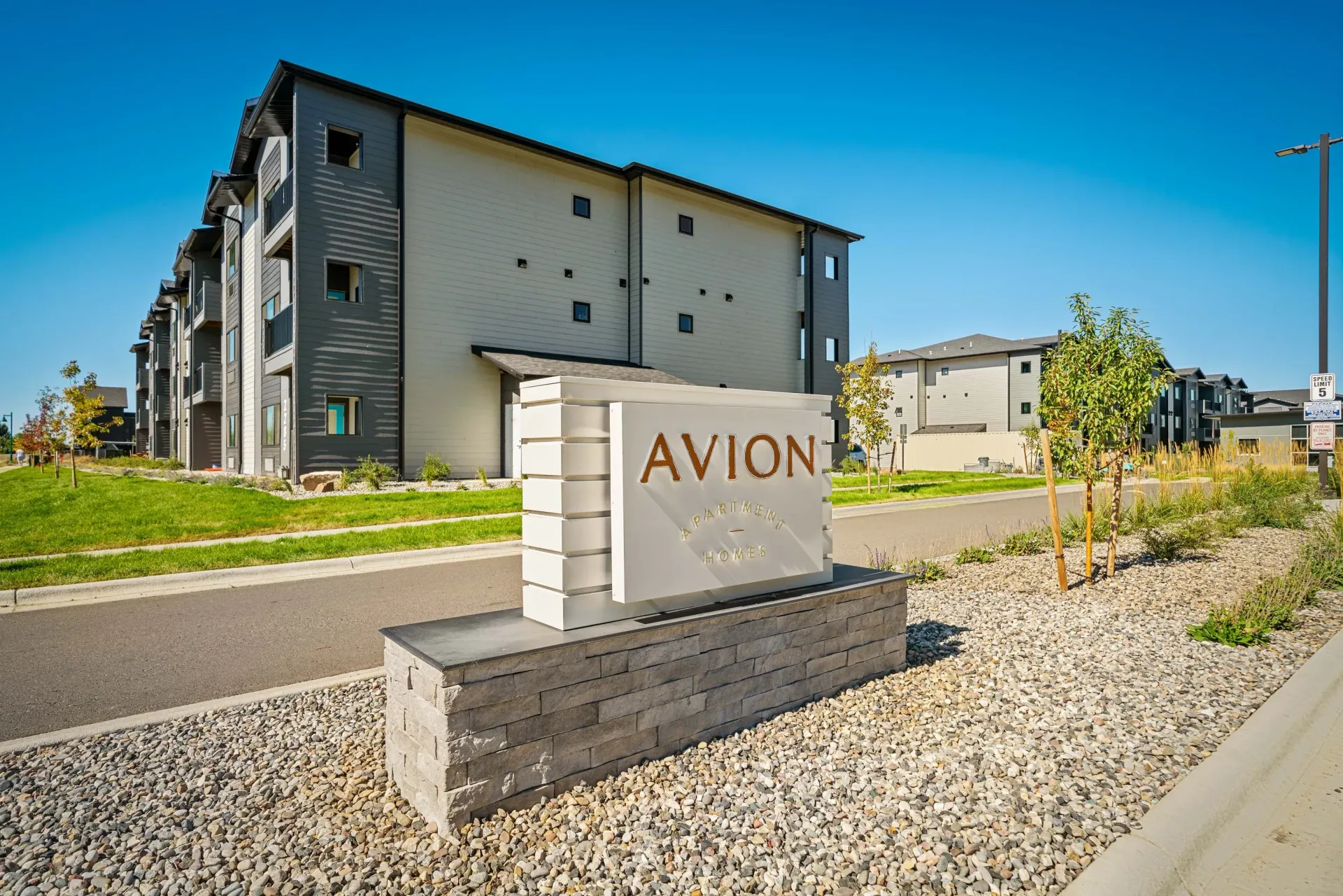 Exterior view of Avion Apartments with multi-story buildings and a landscaped entrance sign.