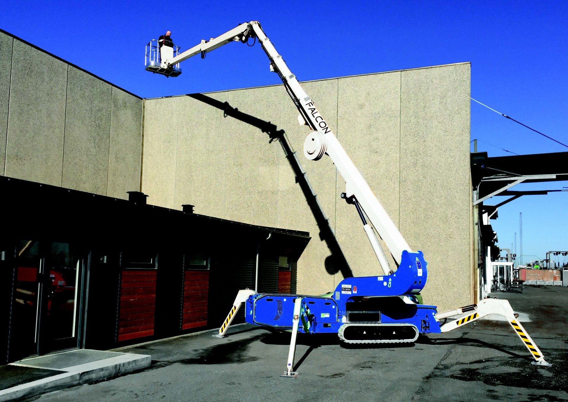 A blue and white spider lift is parked in front of a building