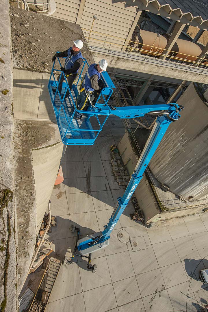 A couple of men are standing in a bucket on top of a crane.
