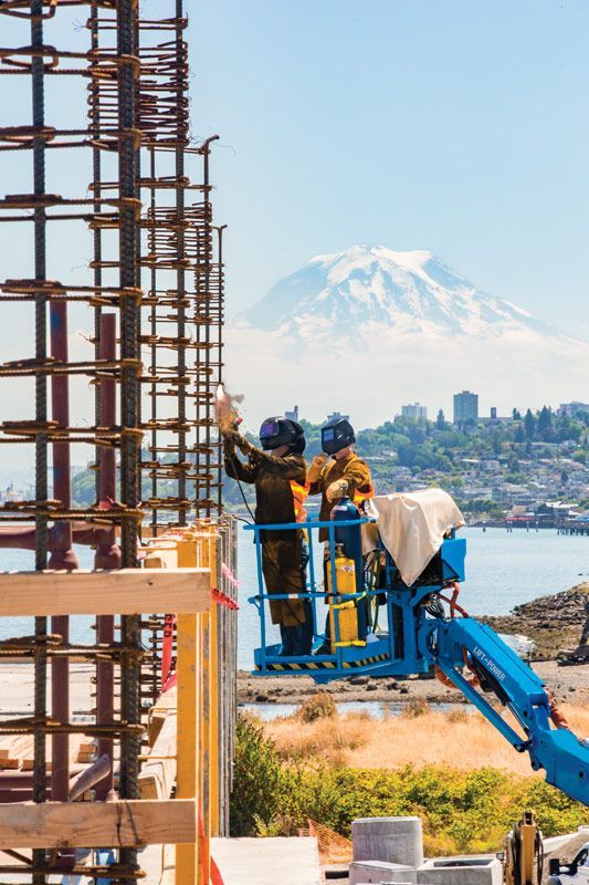 Two construction workers are working on a building with a mountain in the background.