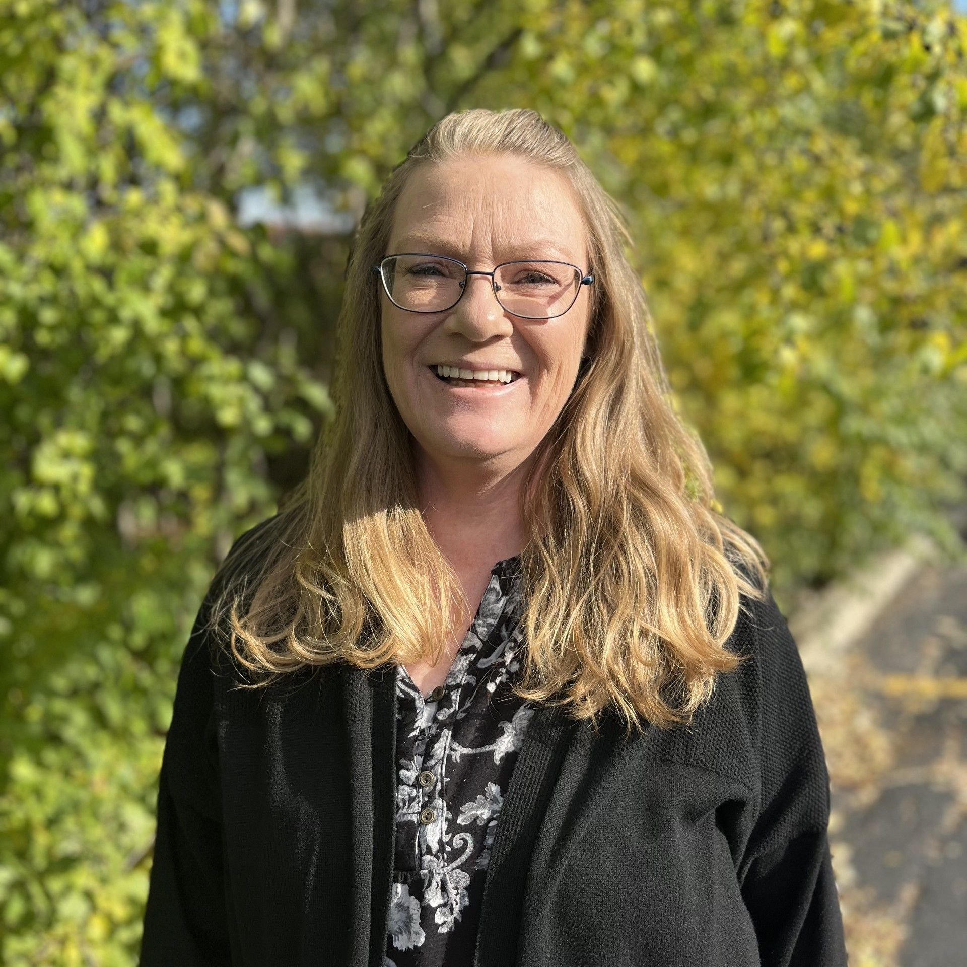 A woman wearing glasses and a black jacket is smiling for the camera.