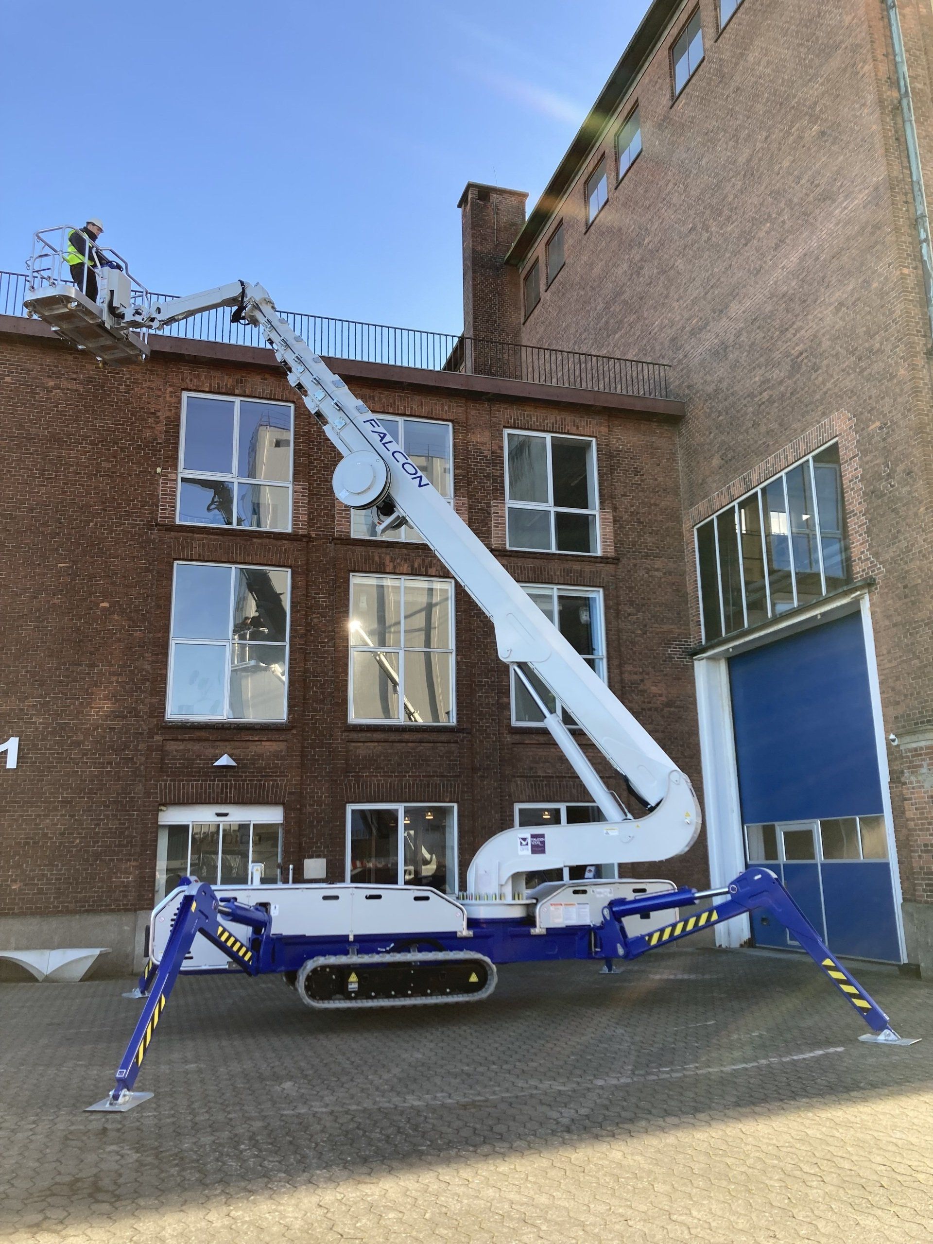 A blue and white crane is parked in front of a brick building