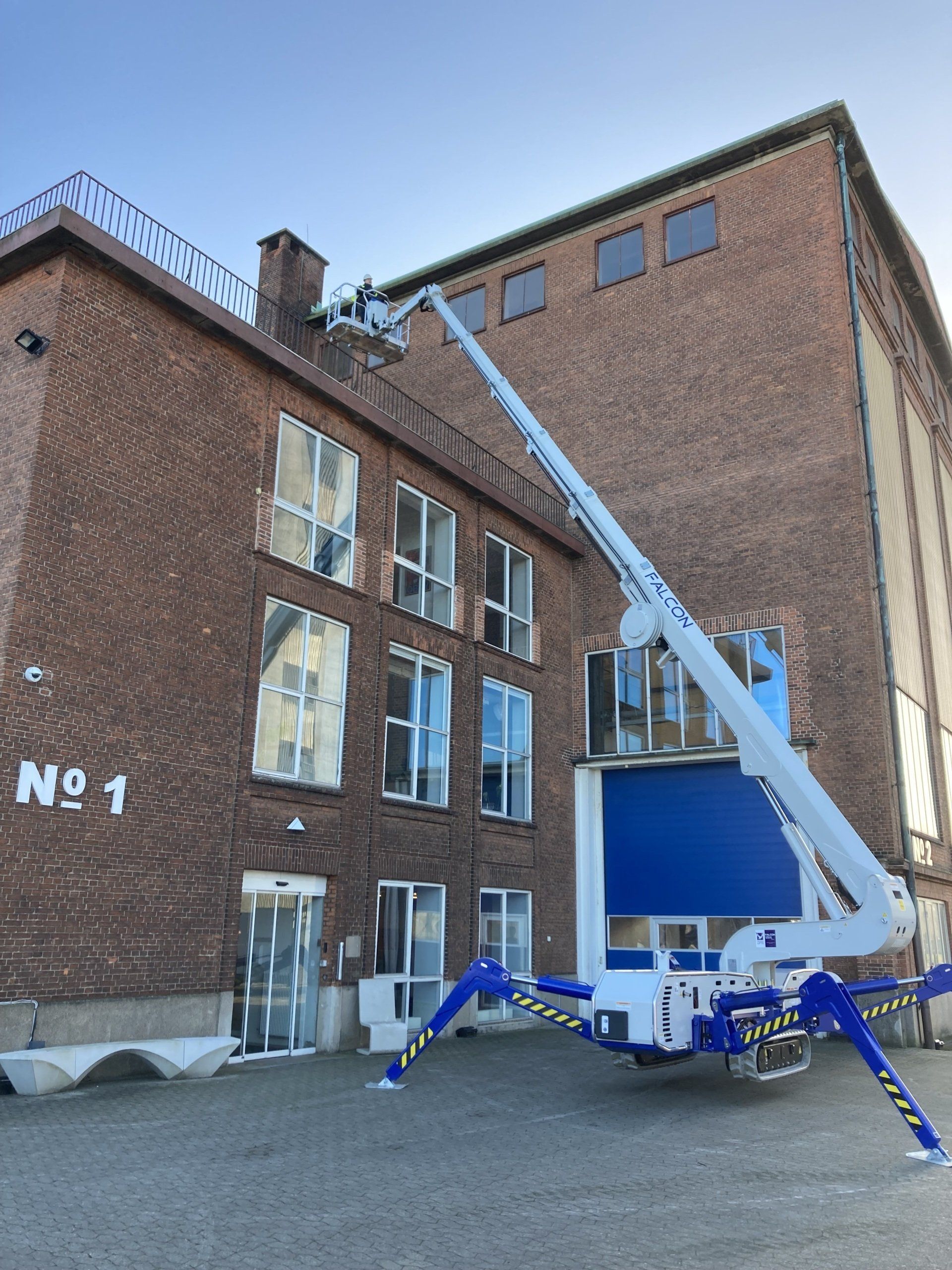 A spider lift is parked in front of a large brick building.