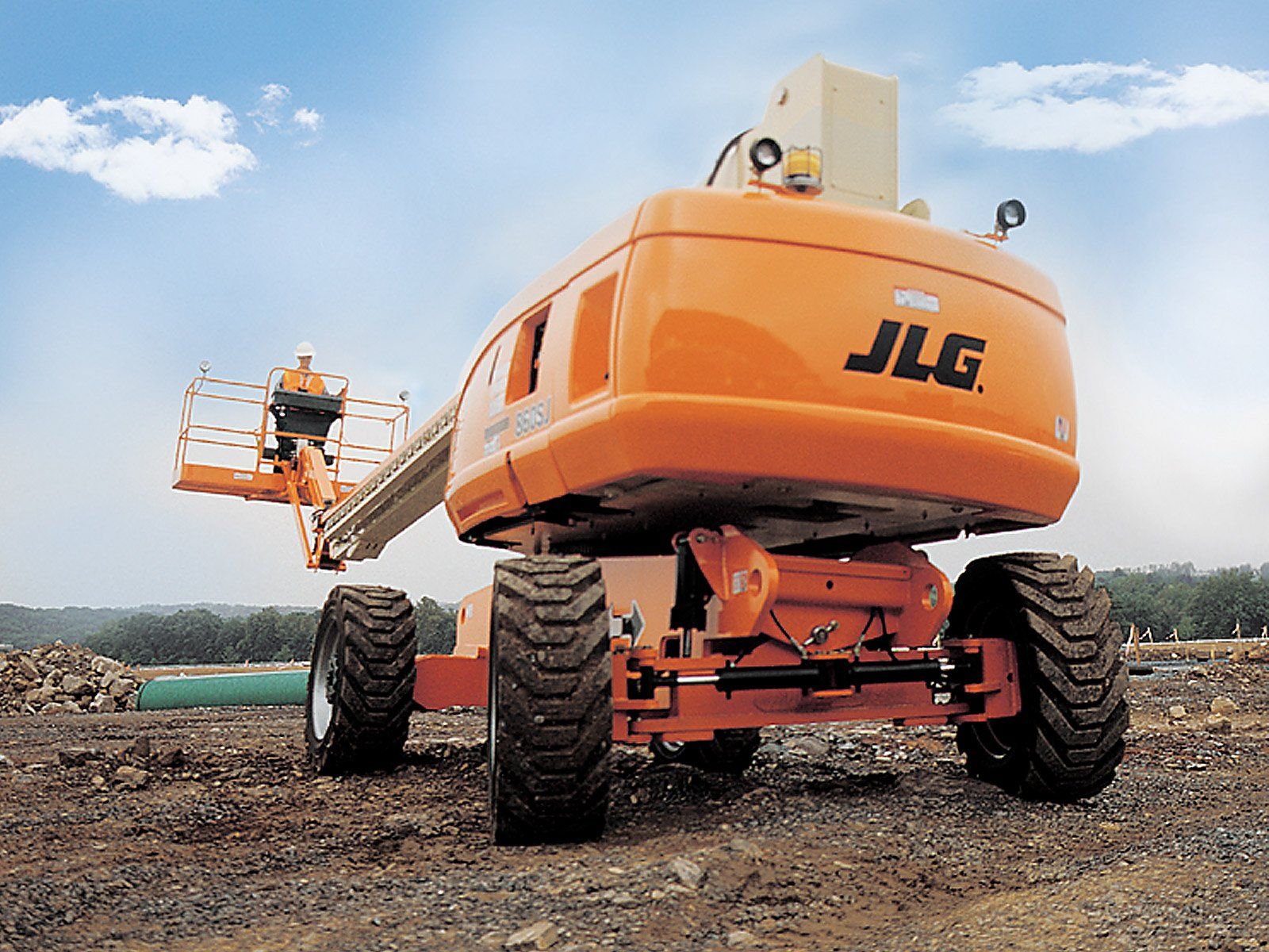 An orange jlg lift is parked in a dirt field