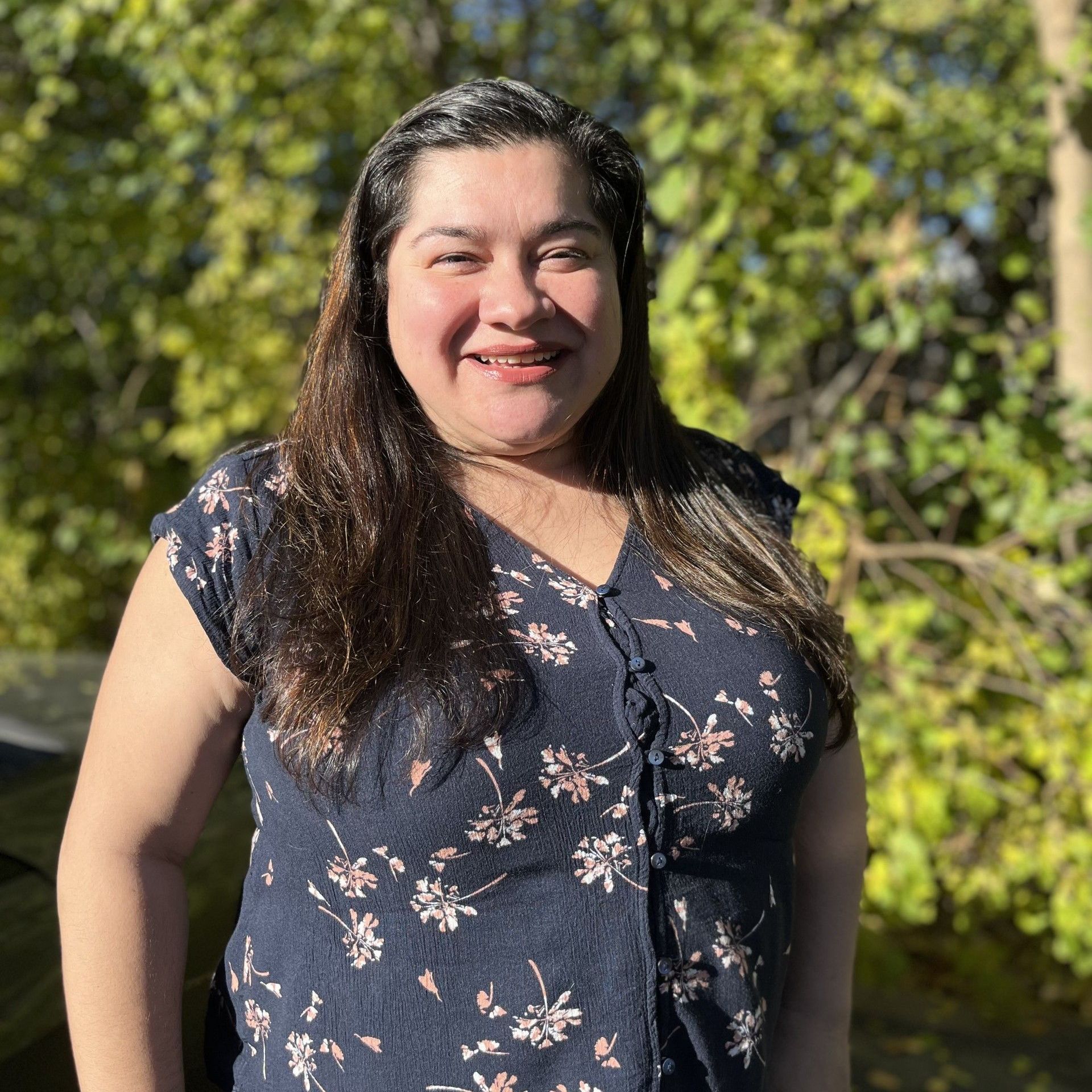 A woman in a blue floral shirt is smiling for the camera.