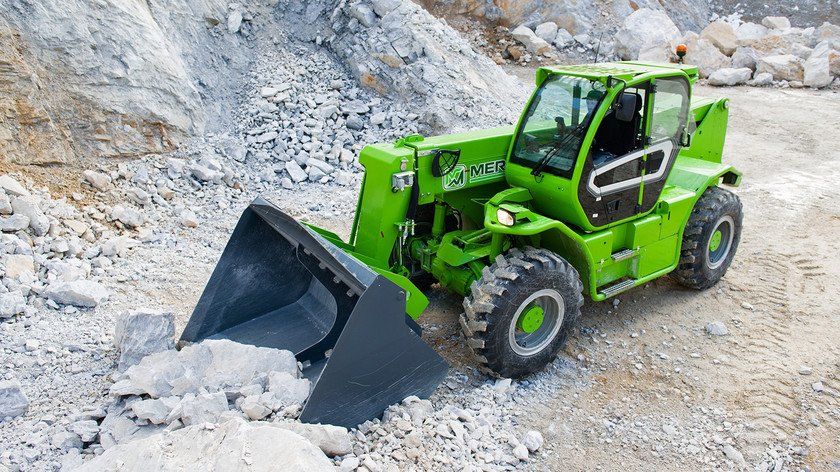 A green forklift with a large bucket is driving down a dirt road.