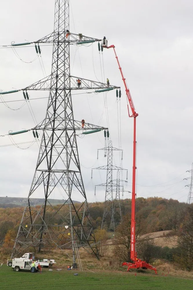 A red crane is working on a power tower