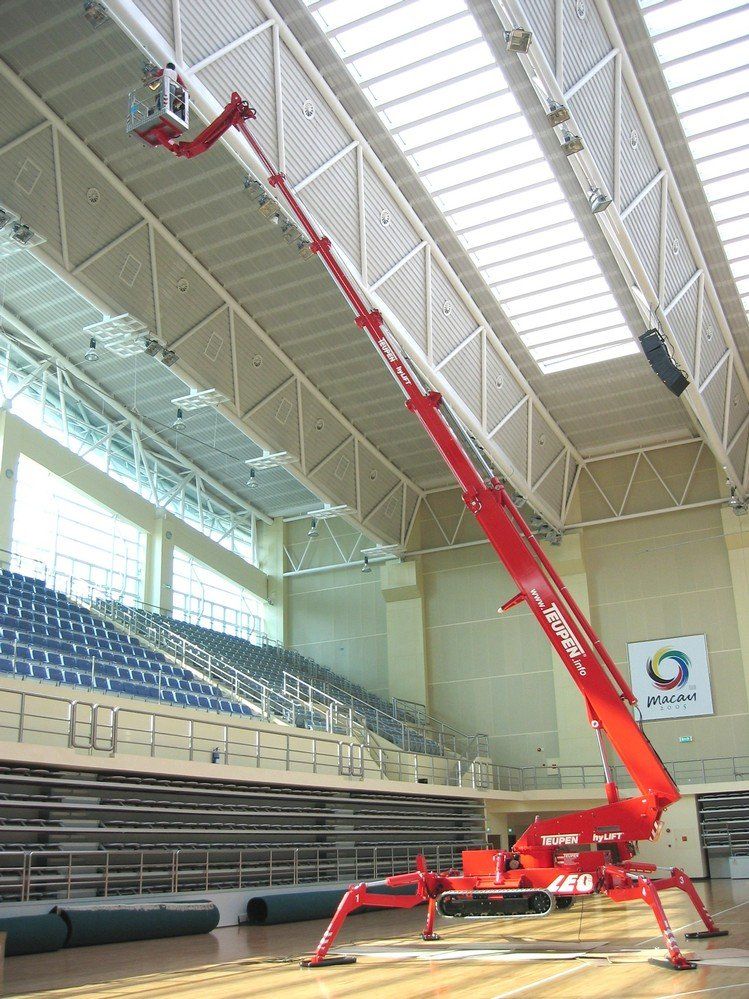 A red crane is sitting in the middle of a basketball court.