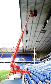 A red crane is working on the ceiling of a stadium.
