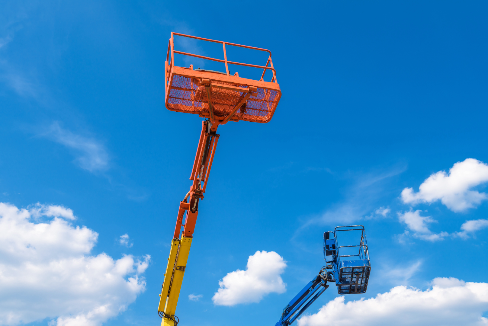 Cherry pickers on blue sky background, lift buckets of heavy machinery Genie and JLG