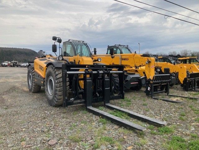 A row of yellow forklifts are parked in a gravel lot.