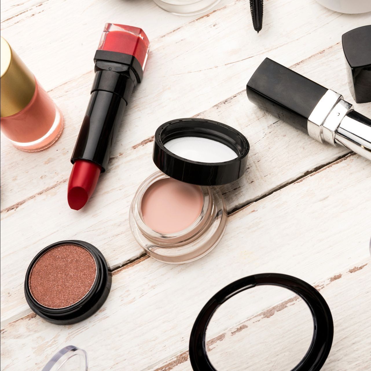A variety of makeup products are laid out on a wooden table