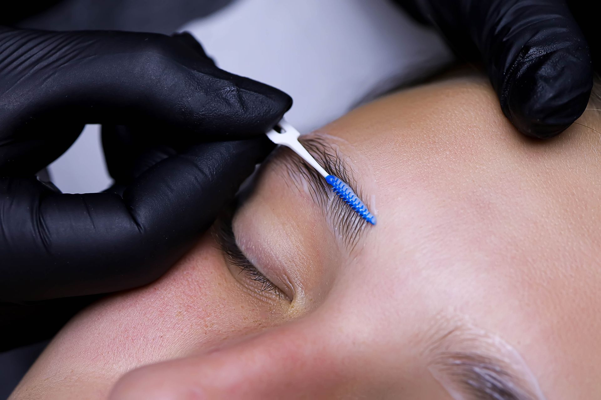 A person is cleaning a woman 's eyebrows with a blue brush.