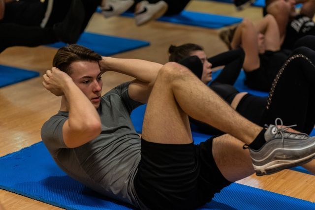 Een groep mensen doet crunches op blauwe matten in een sportschool.