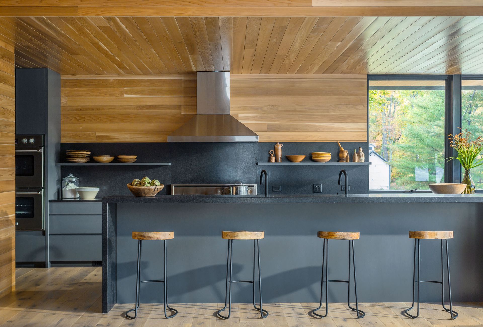 A kitchen with a large island and stools and a wooden ceiling.