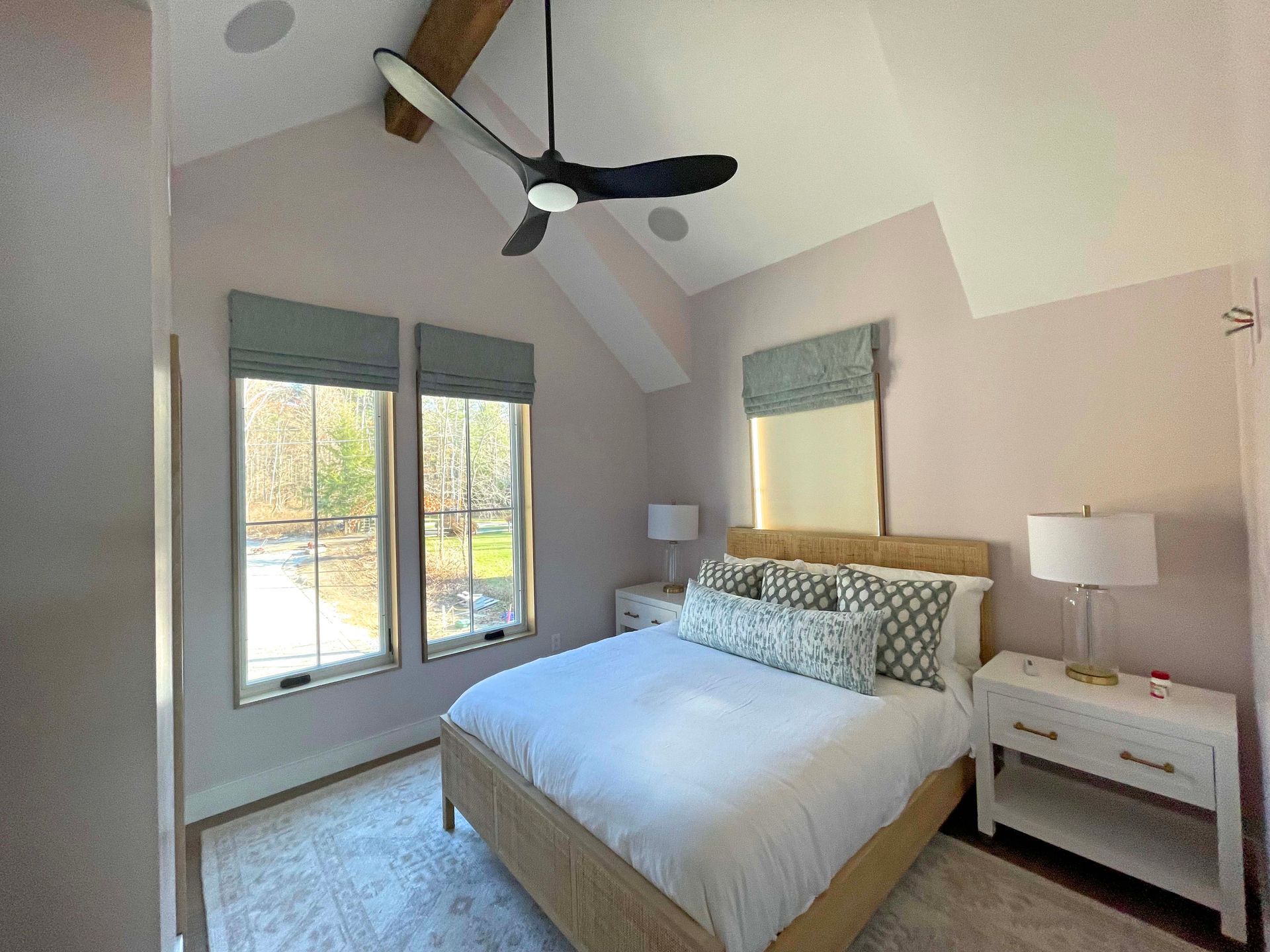 A bedroom with a bed , nightstands , a ceiling fan and two windows.
